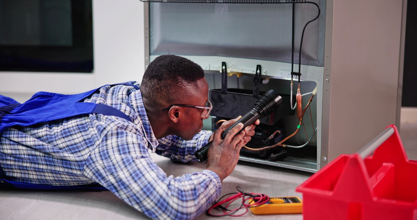 Um homem está deitado no chão consertando uma geladeira.